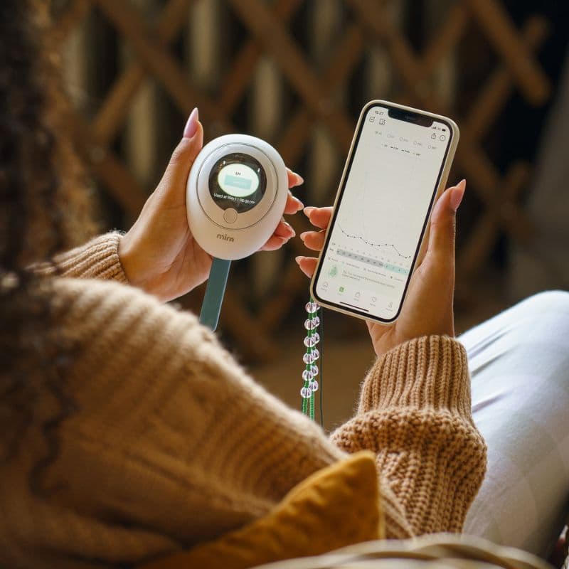 Frau hält einen digitalen Hormonmonitor in der Hand und betrachtet die Hormonverlaufskurve in einer App auf dem Smartphone – Hormontracking zu Hause in den Wechseljahren.